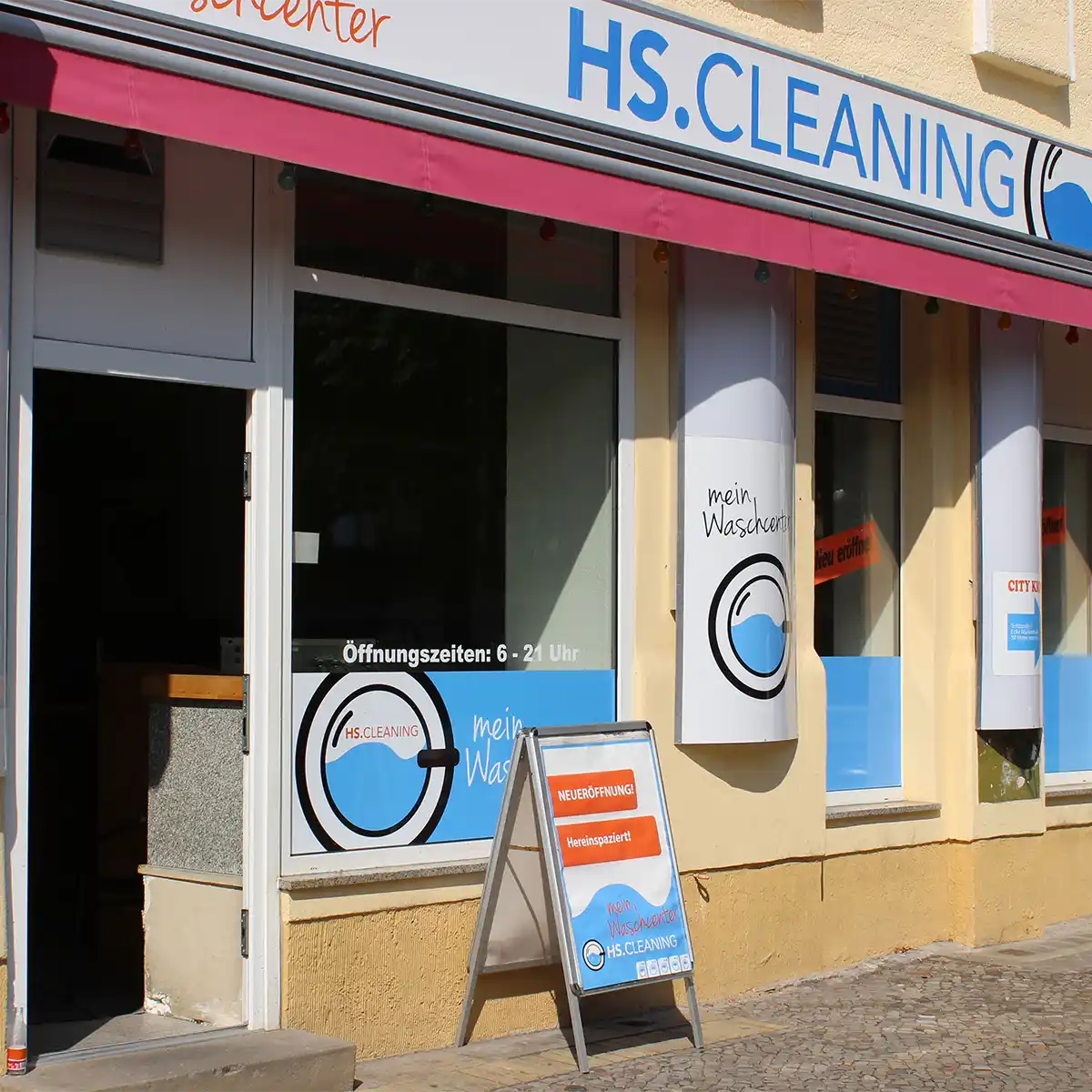 The entrance to the HS.Cleaning washing center. Four shop windows with HS.Cleaning advertising, to the left of which is the entrance