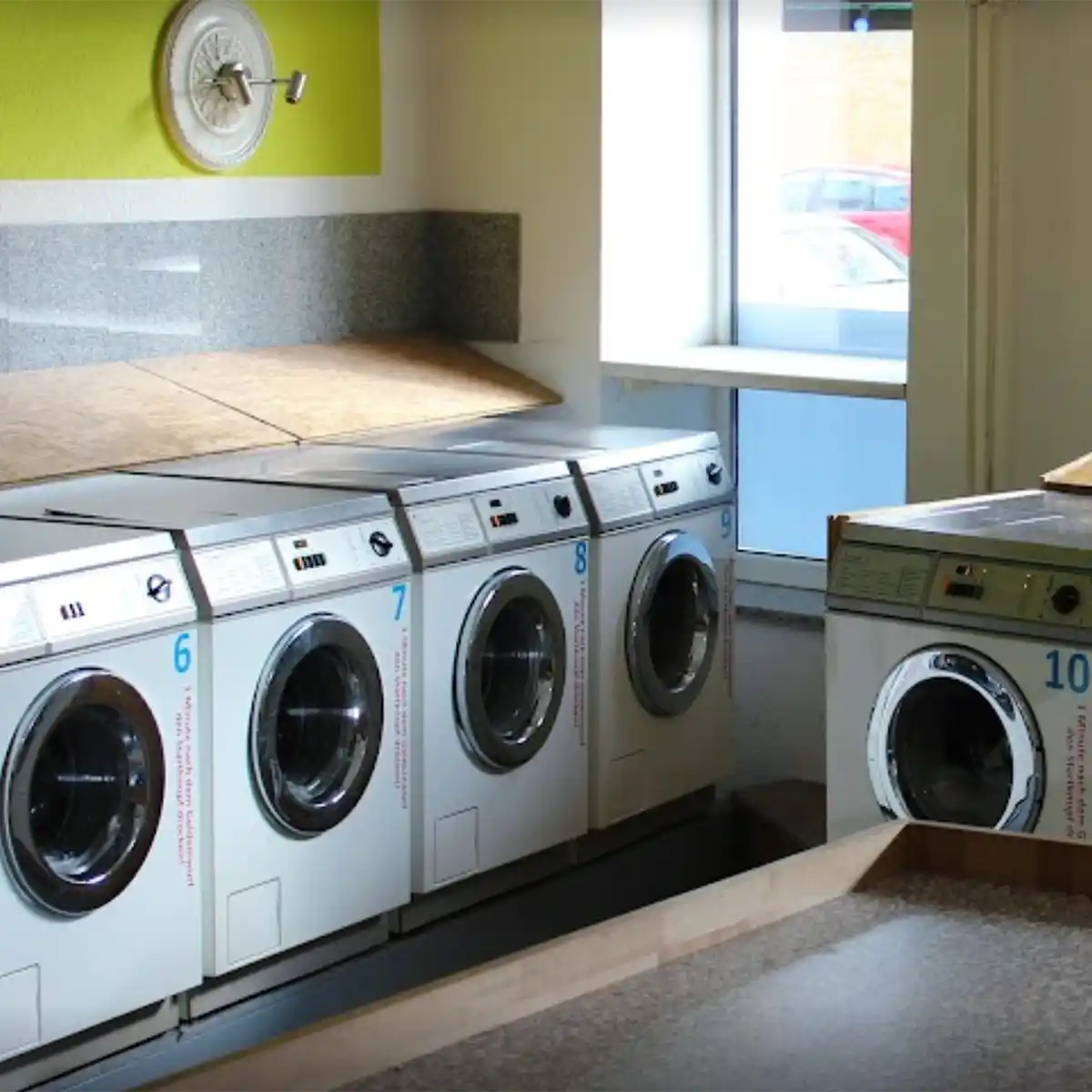 A row of washing machines, each with a large opening with chromed frames